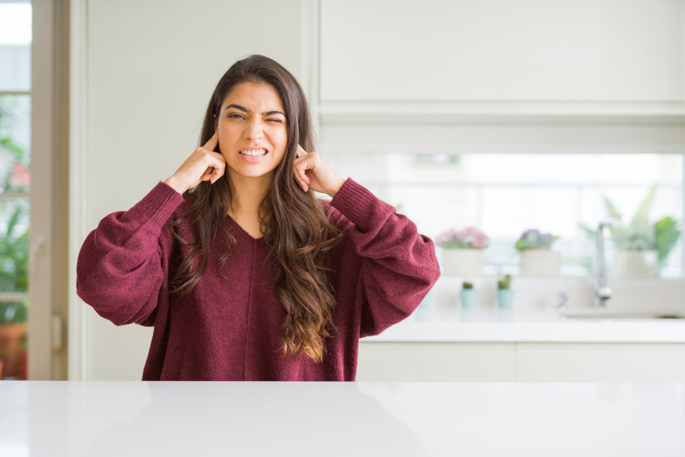 woman at home covering ears with fingers with annoyed expression for the noise of loud music outside
